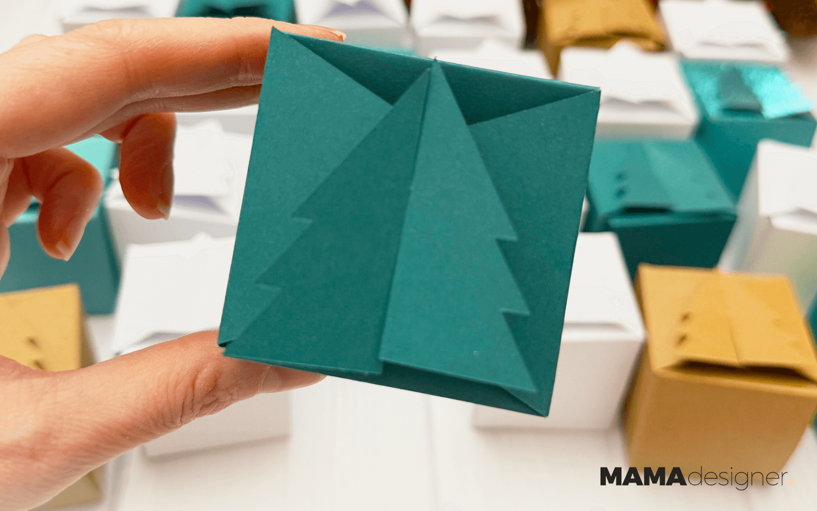 Zbliżenie na zielone pudełeczko z choinką. W tle pozostałe 24 pudełeczka kalendarza adwentowego.