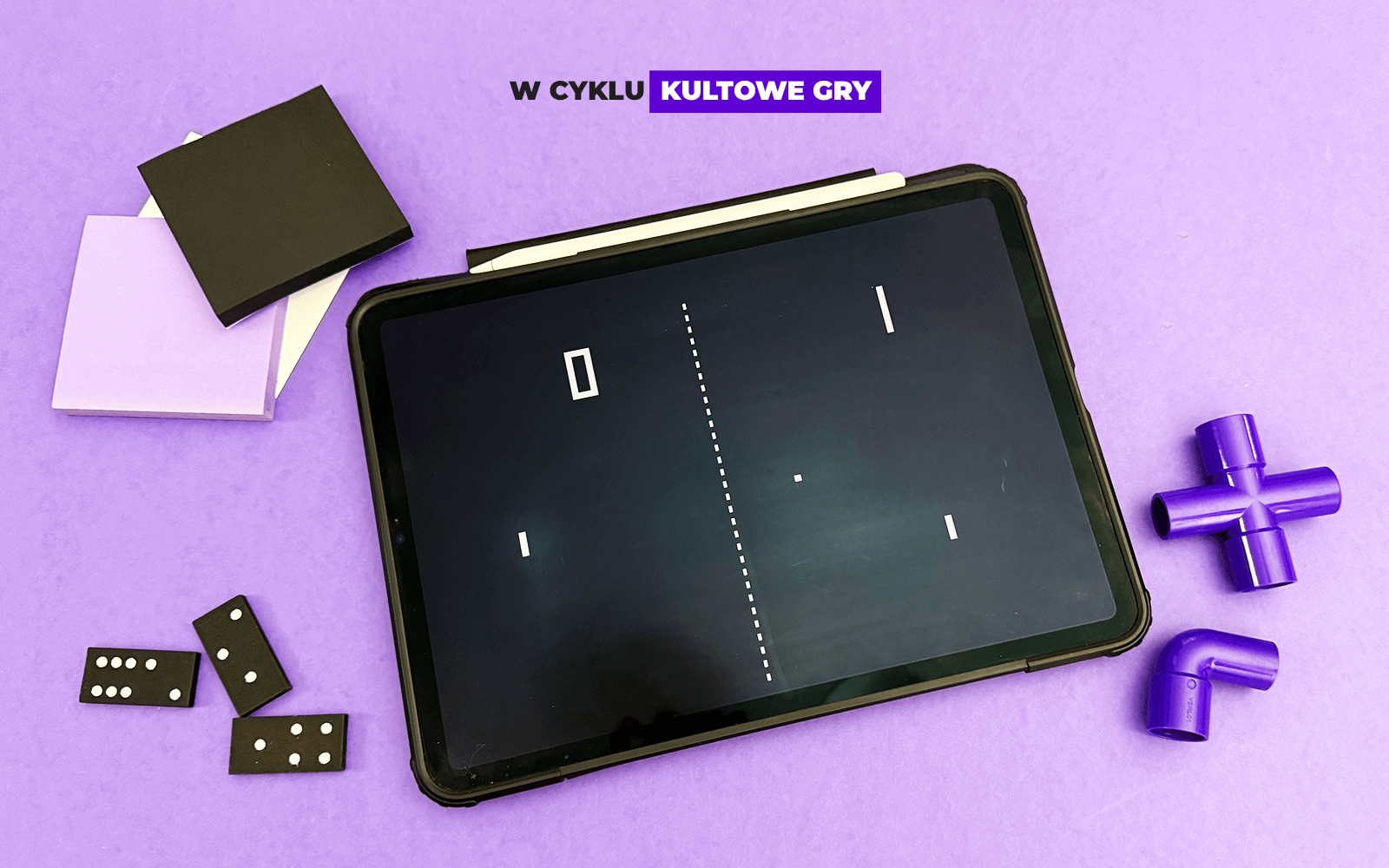 Tablet pokazujący zrzut z gry Pong. Tablet leży na fioletowym tle, dookoła leżą fioletowe i czarne obiekty, takie jak kostki domino, czy klocki rury.