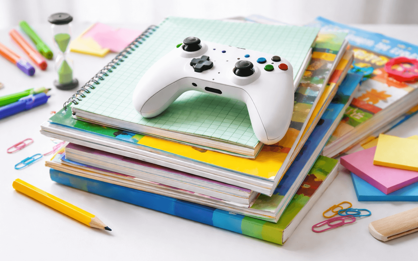 Kontroler do gry leży na stosie podręczników i ćwiczeniówek z pracą domową.