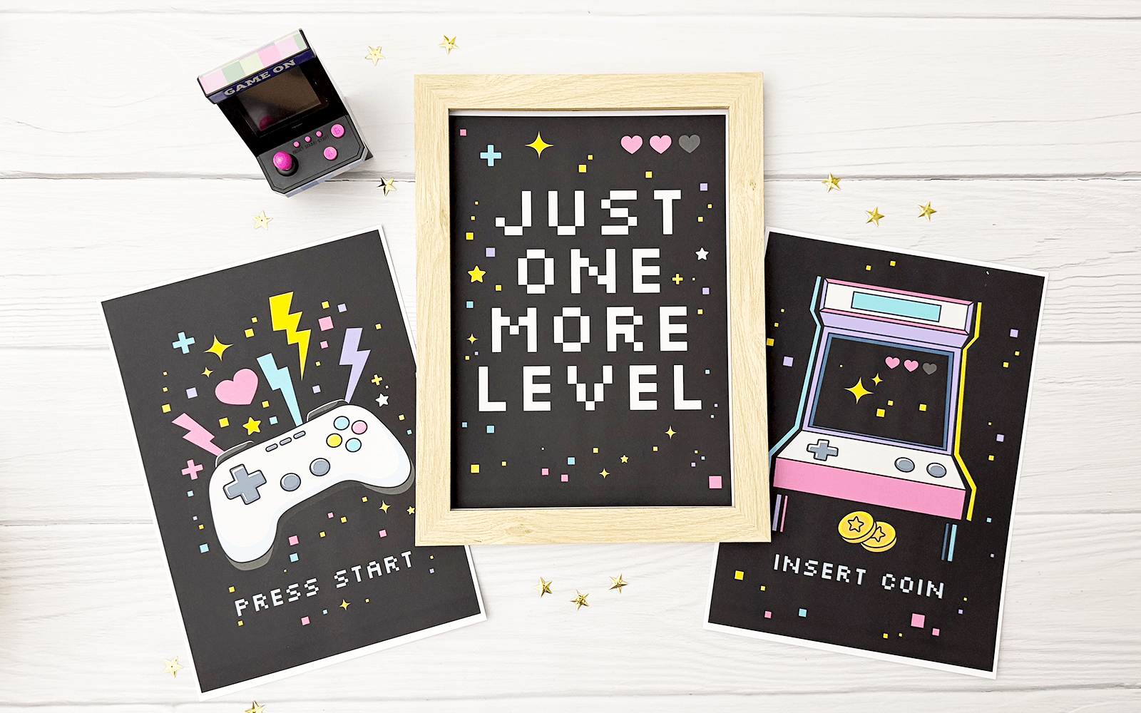 Retro gamingowy zestaw plakatów: Press Start, Just One More Level i Insert Coin. Plakaty mają czarne tło i ilustracje składające się z neonowych, żywych kolorów: magenta, cyjan, żółty i fiolet.